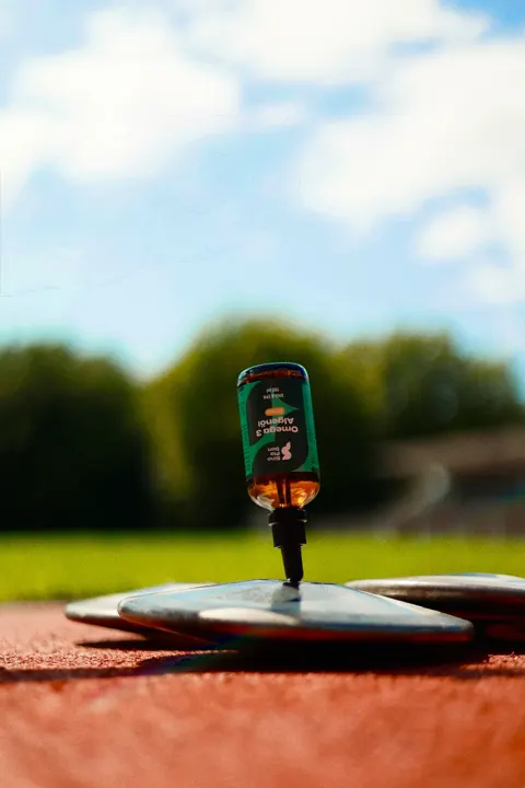 Flasche SinoPlaSan Omega-3-Algenöl steht auf einem Diskus im Stadion
